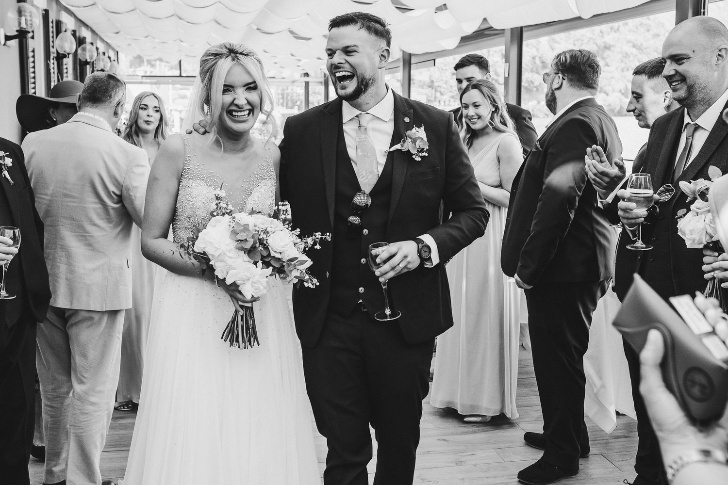 A black and white capture of newlyweds sharing laughter with their wedding guests.