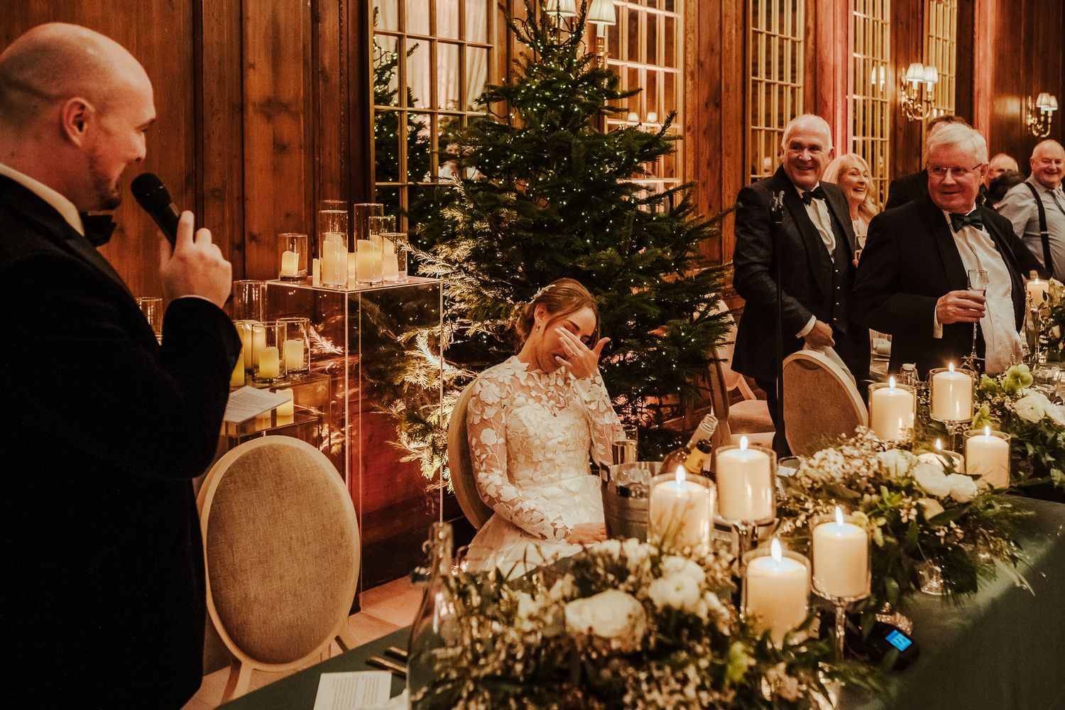 Elegantly decorated wedding reception with Christmas tree and candlelit table settings in rustic wooden venue.