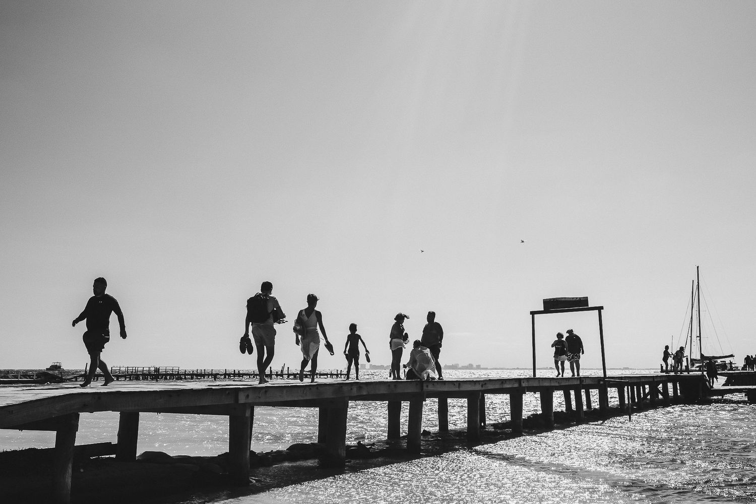 Silhouettes of people walking on a pier at sunset.