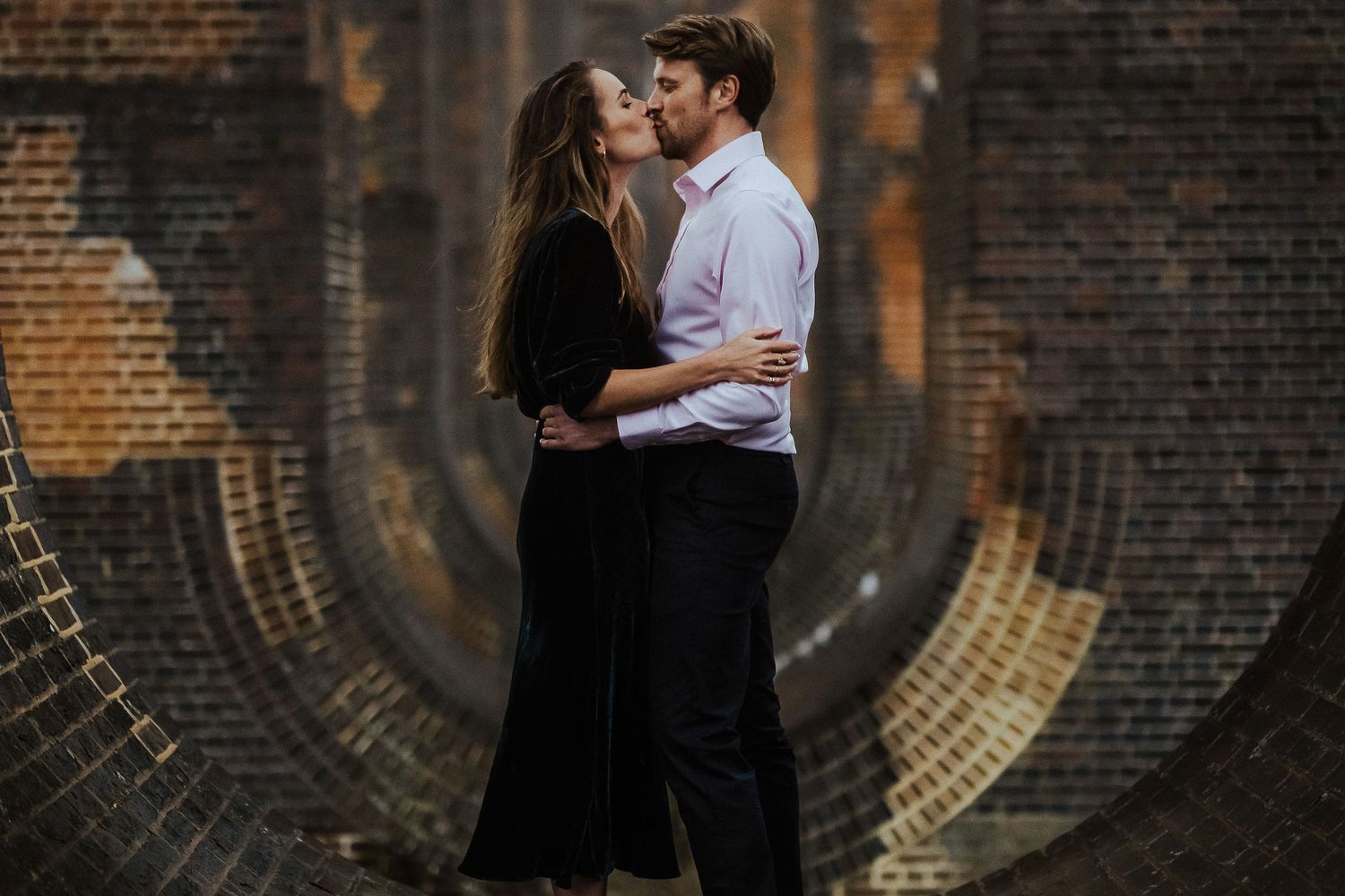 Couple sharing an intimate moment in a dramatic brick tunnel setting.