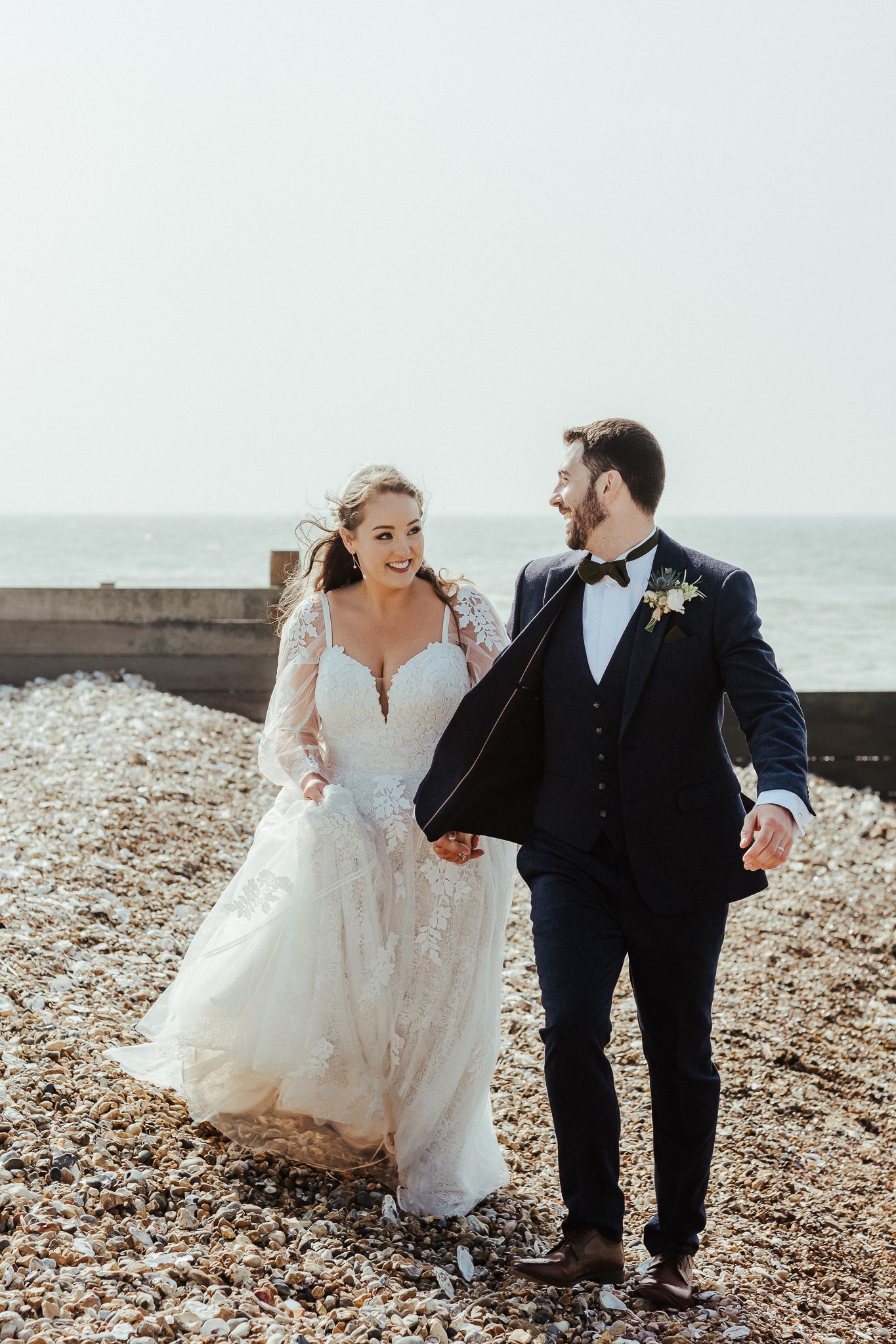 Bride and groom walking together on a rocky beach during their coastal wedding.
