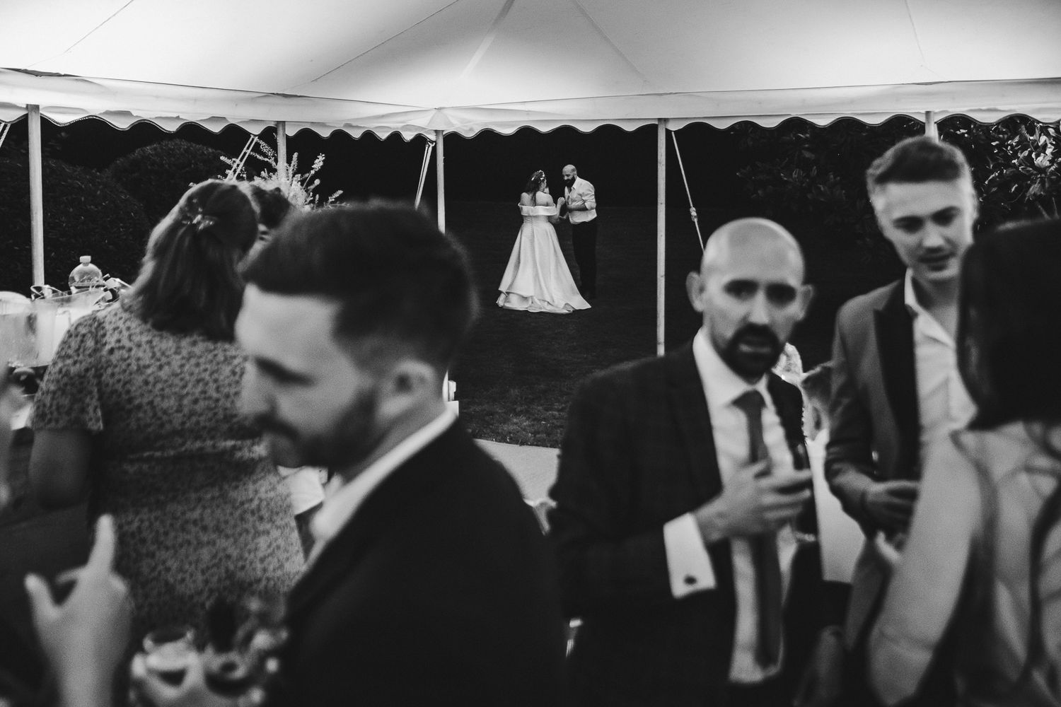 Wedding guests dancing and celebrating on a dimly lit dance floor at an evening reception.