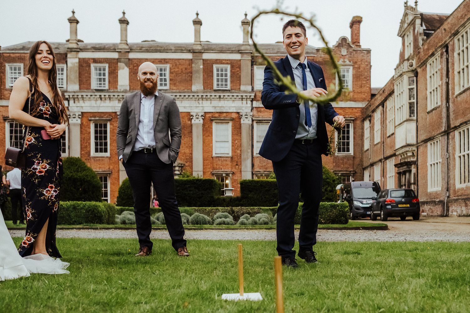 Wedding guests play lawn games including croquet outside a historic brick mansion.