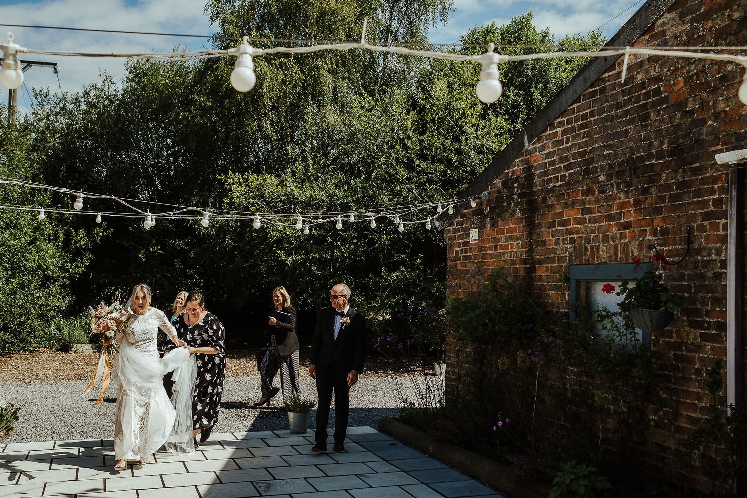 Outdoor wedding ceremony setup with string lights and brick wall backdrop.