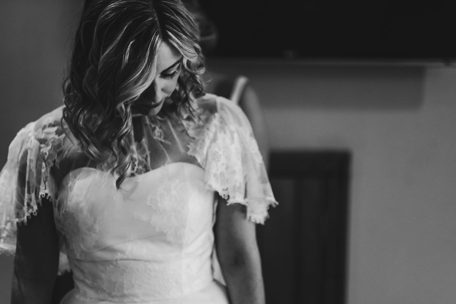 Black and white portrait of bride in lace wedding dress looking down.