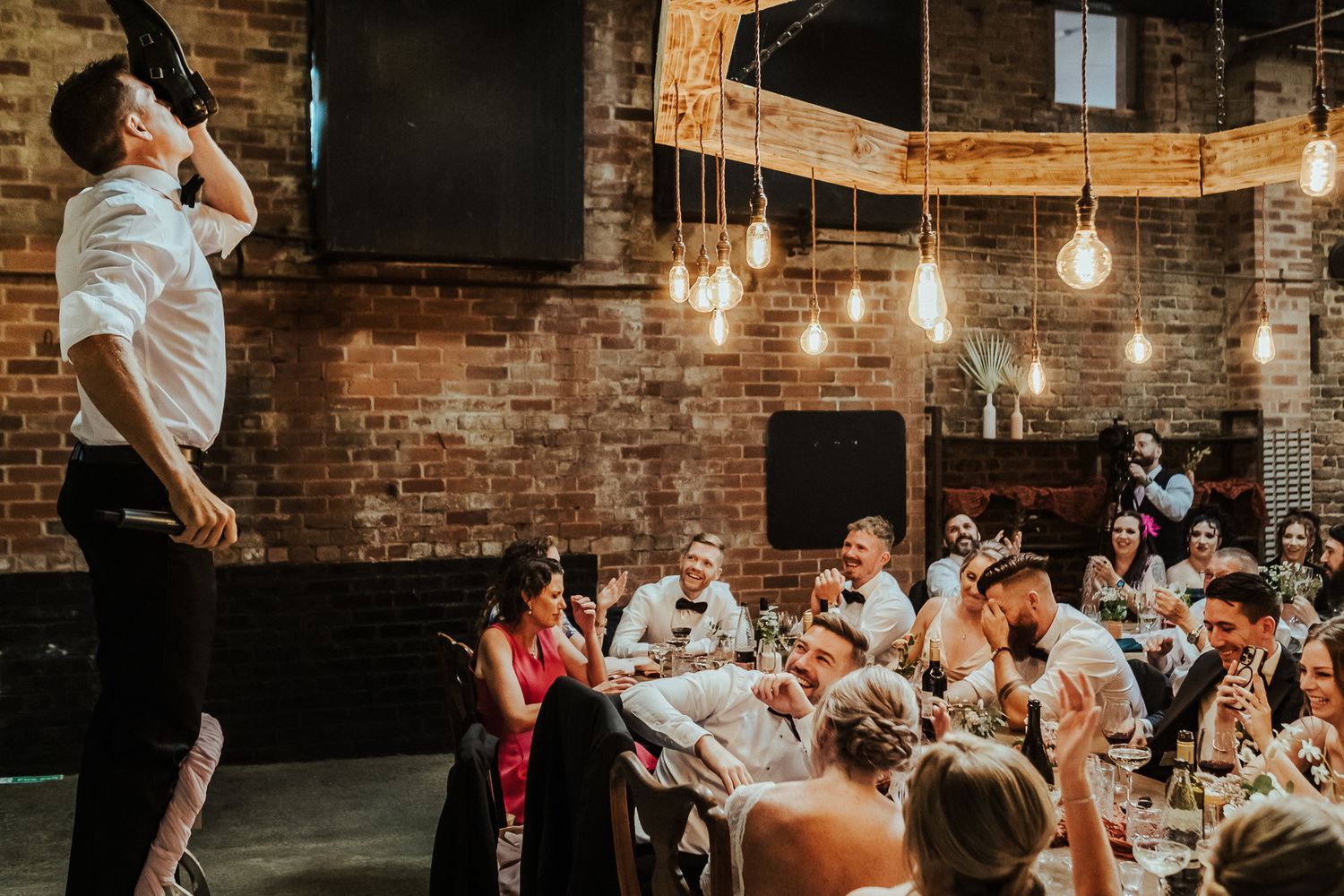Reception celebration in industrial brick venue with hanging Edison bulbs.