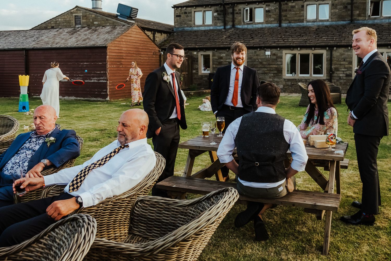 Wedding guests relax at outdoor picnic tables during a reception.