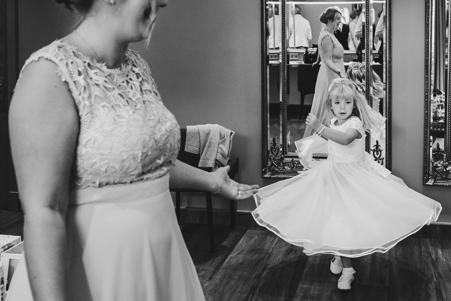 Black and white photo capturing a sweet moment between a flower girl twirling in her dress.