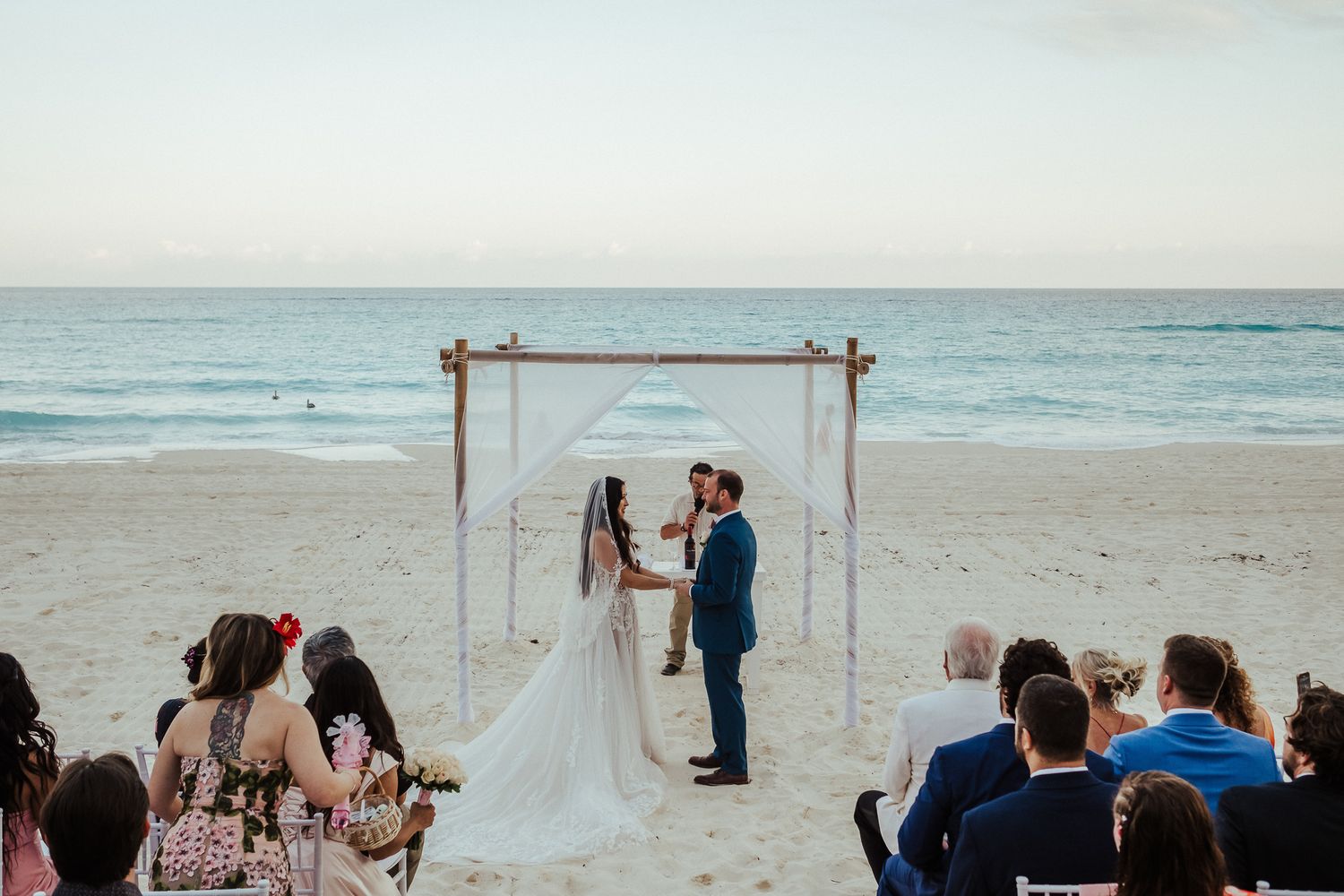 Beachfront wedding ceremony under a simple arch at sunset with ocean views.
