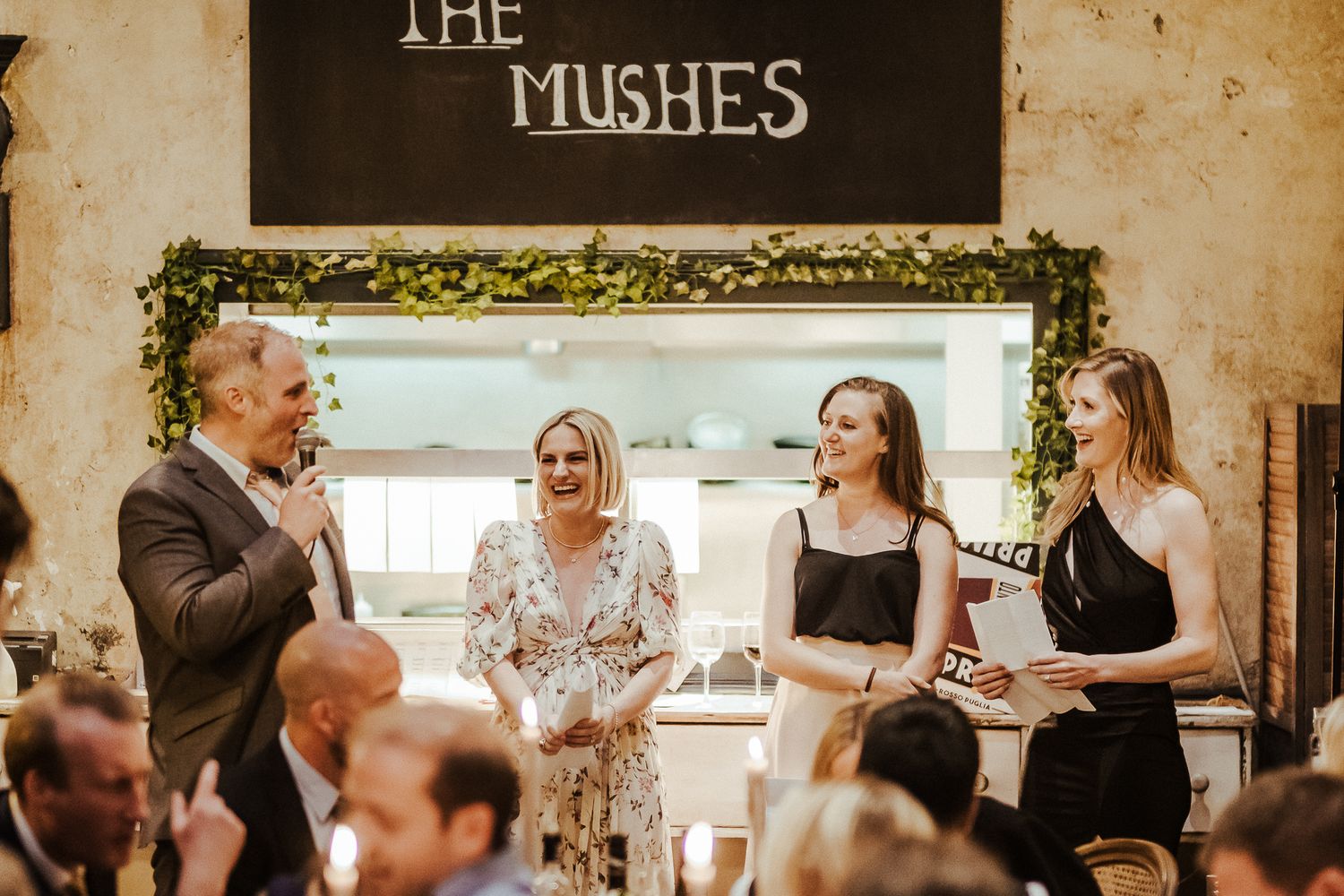 Wedding guests gather beneath 'The Mushes' sign for celebratory toasts.