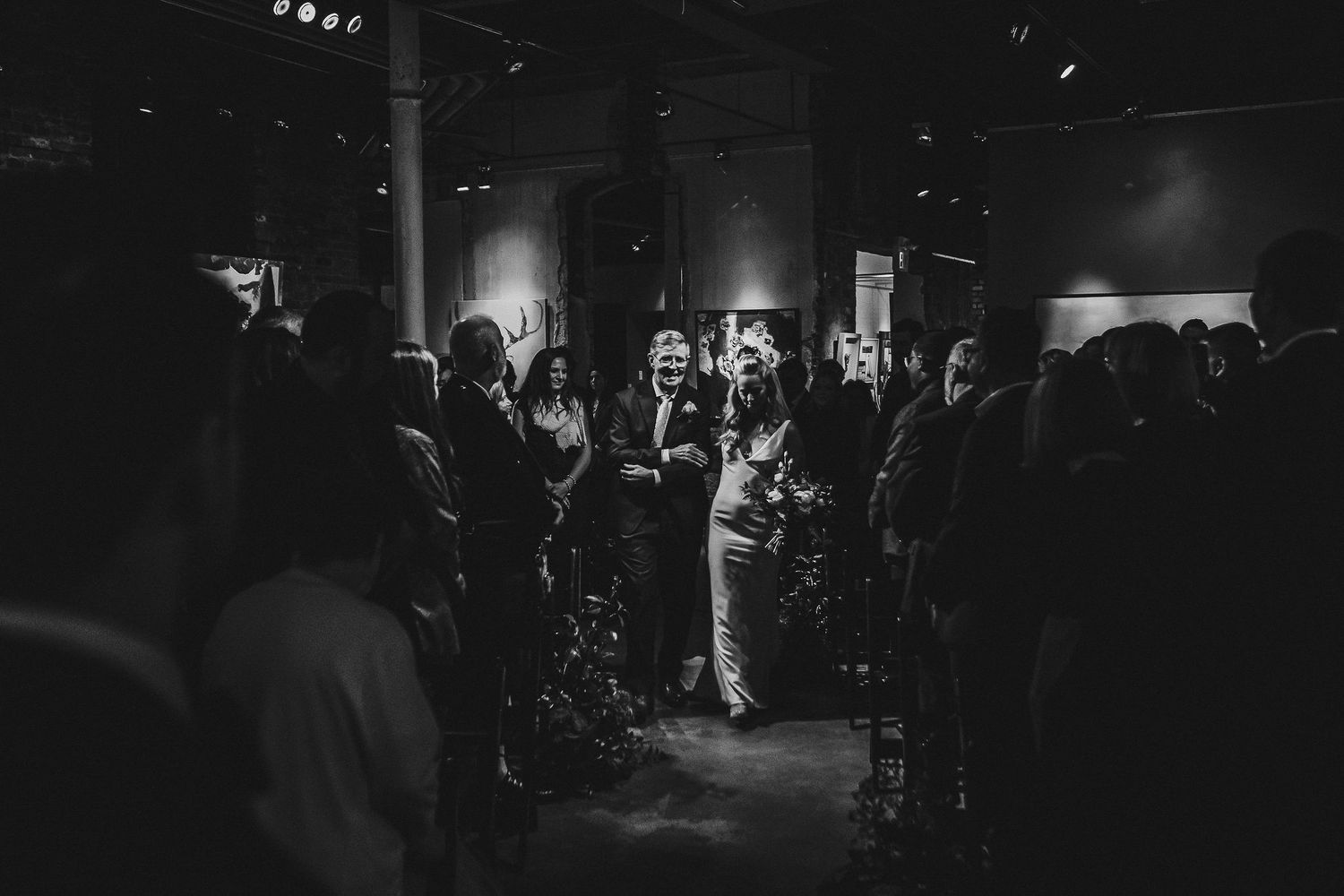 Silhouettes of wedding guests mingling during evening reception in dark venue.