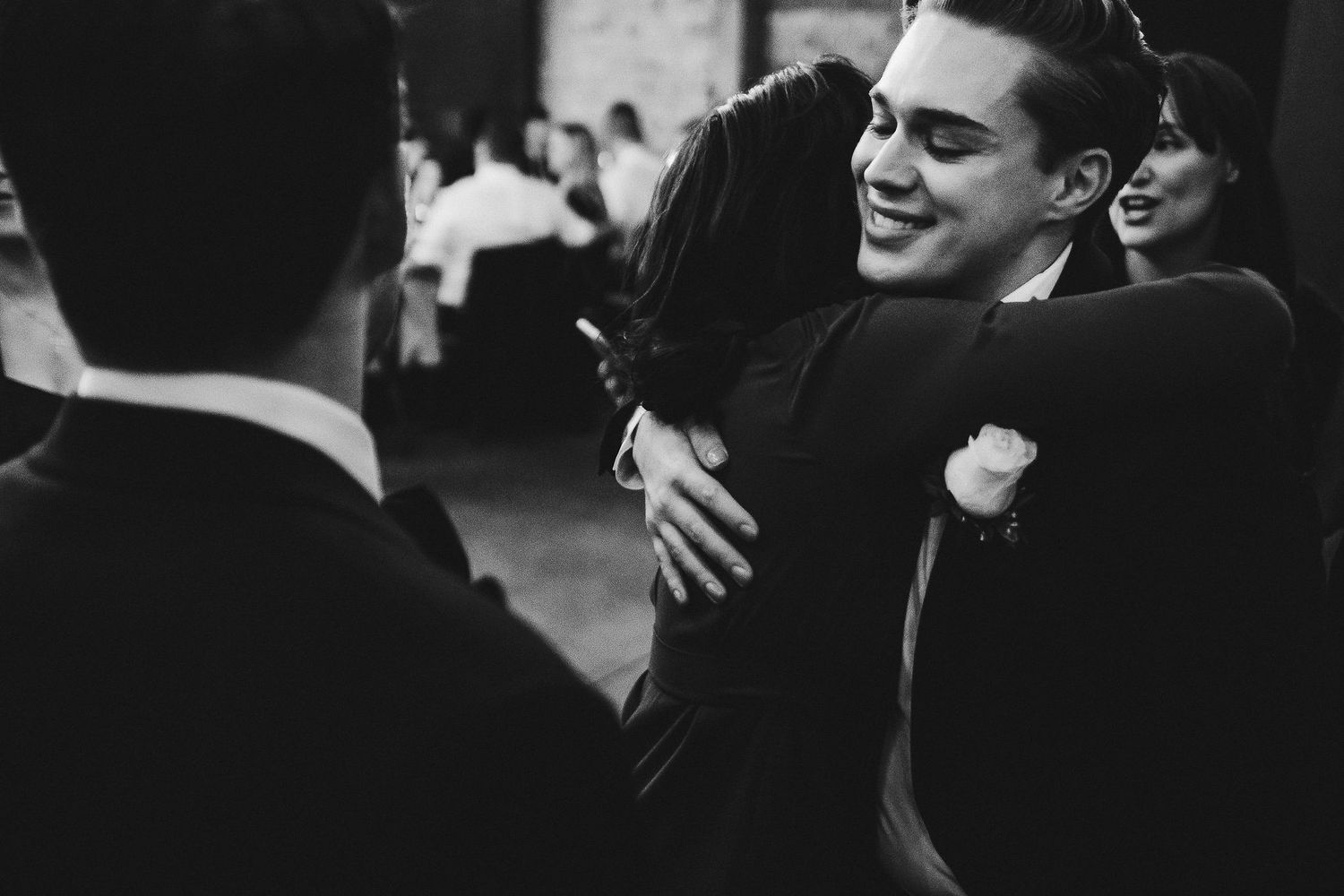 Black and white photo captures joyful embraces at formal celebration.