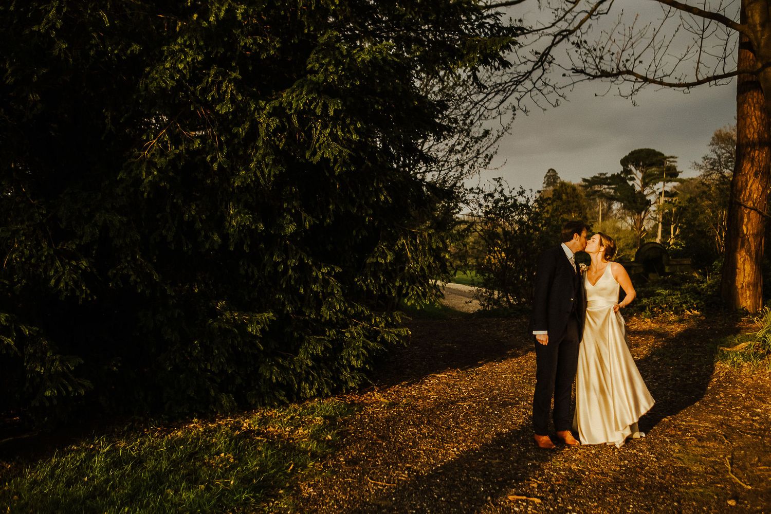 Silhouettes of a couple pose against a dramatic sunset backdrop in a rustic outdoor setting.