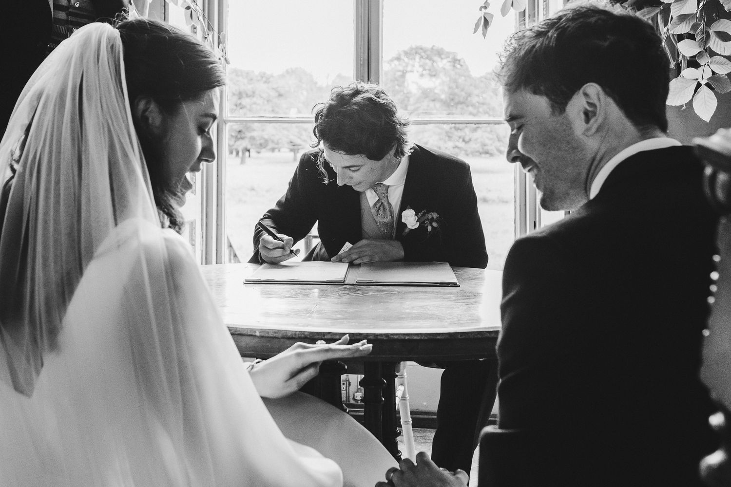 Black and white photo of couple signing marriage documents with officiant.