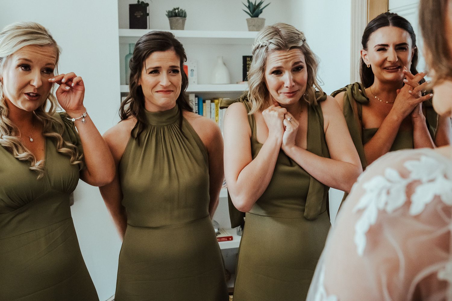 Bridesmaids in matching olive green dresses react emotionally to seeing the bride.