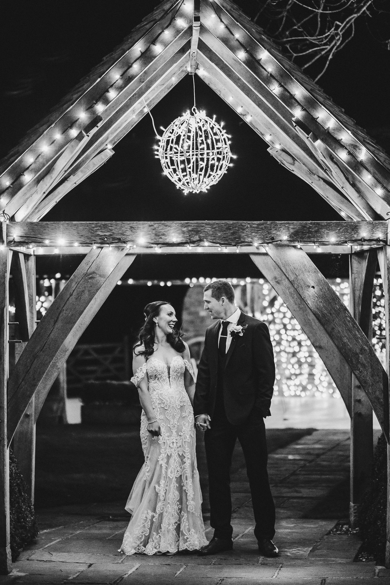 Couple standing under illuminated wooden archway during evening wedding ceremony.
