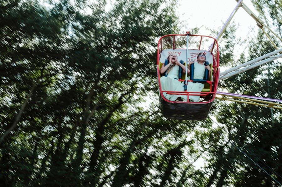 Wedding couple riding in ski lift gondola through green forest canopy.