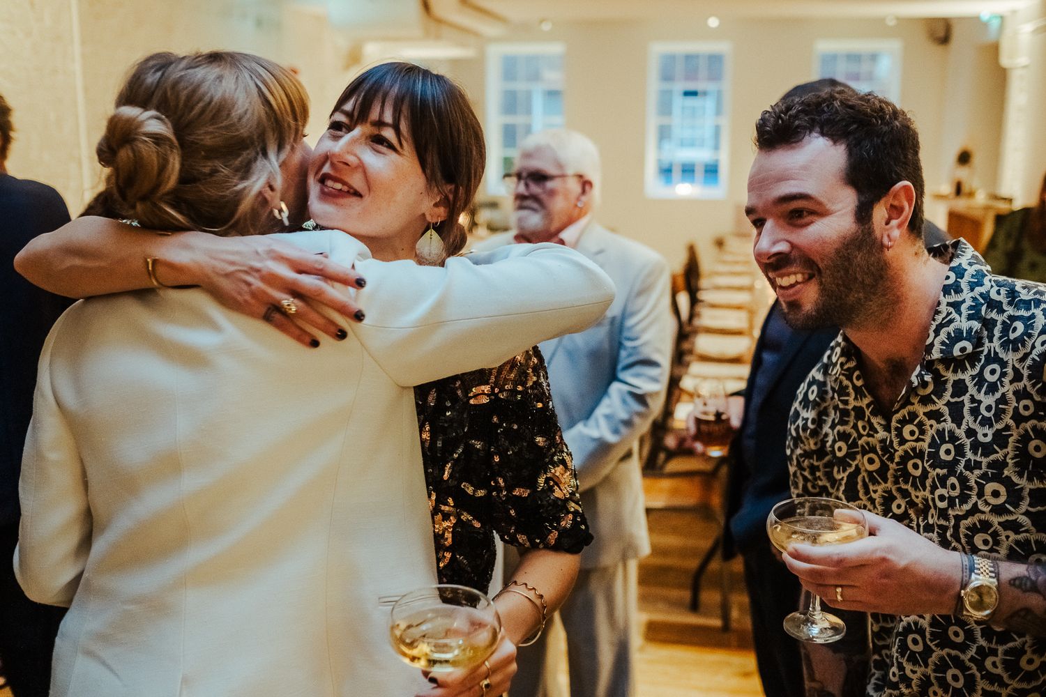 Wedding guests laugh and hug during a reception celebration.