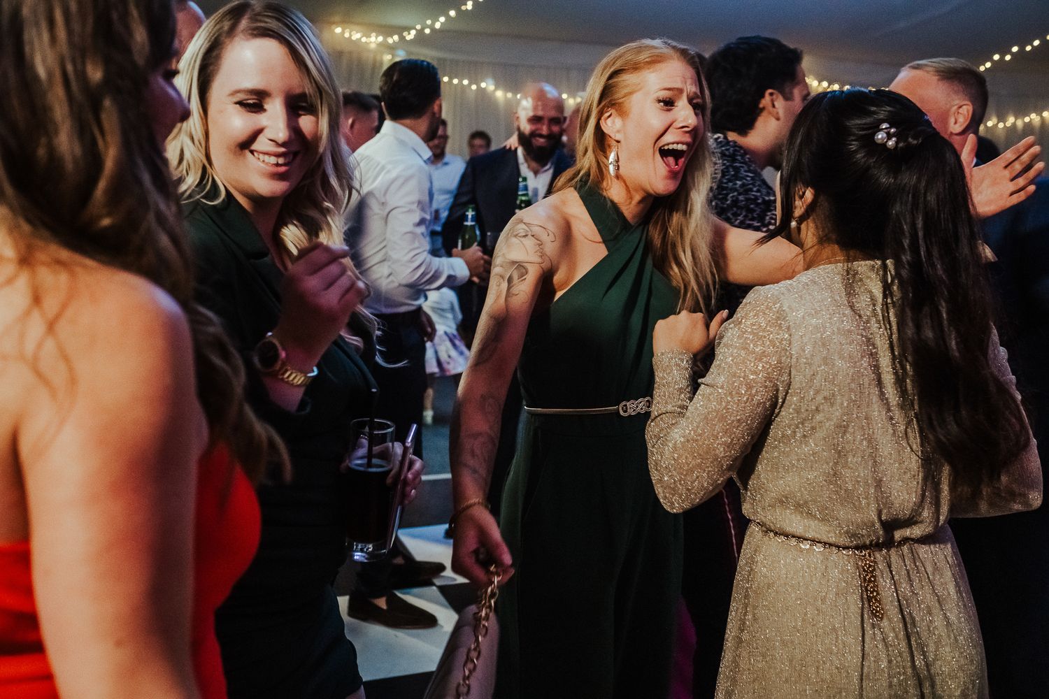 People dancing and socializing at a festive indoor event with string lights hanging overhead.
