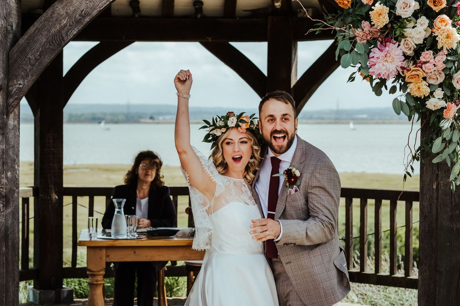 Newlyweds celebrate triumphantly under rustic wooden gazebo with floral decorations.