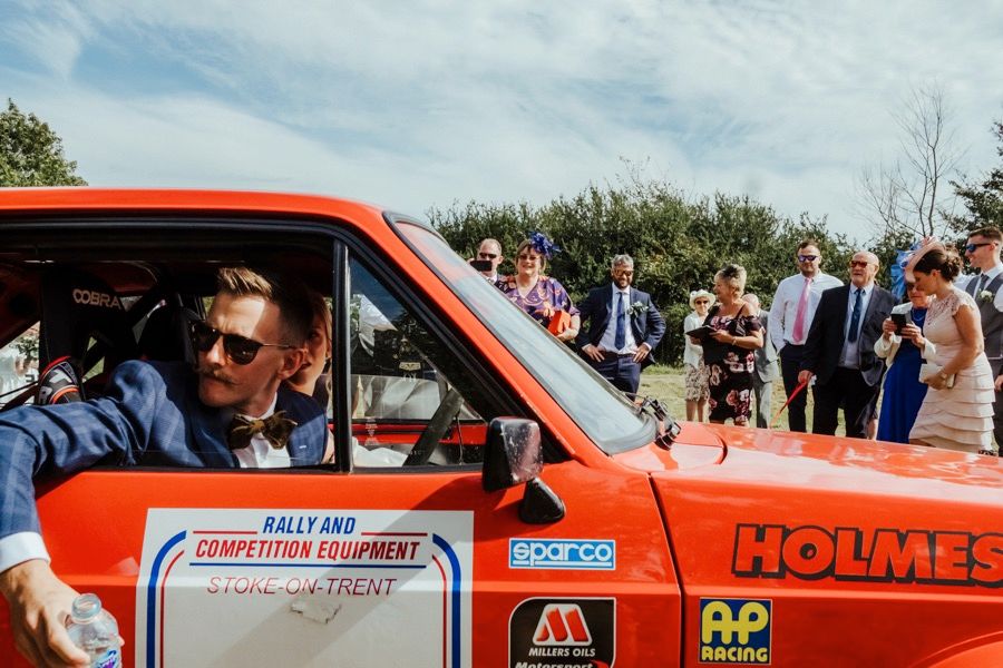 Classic orange vintage rally car decorated for a wedding celebration on a sunny day.