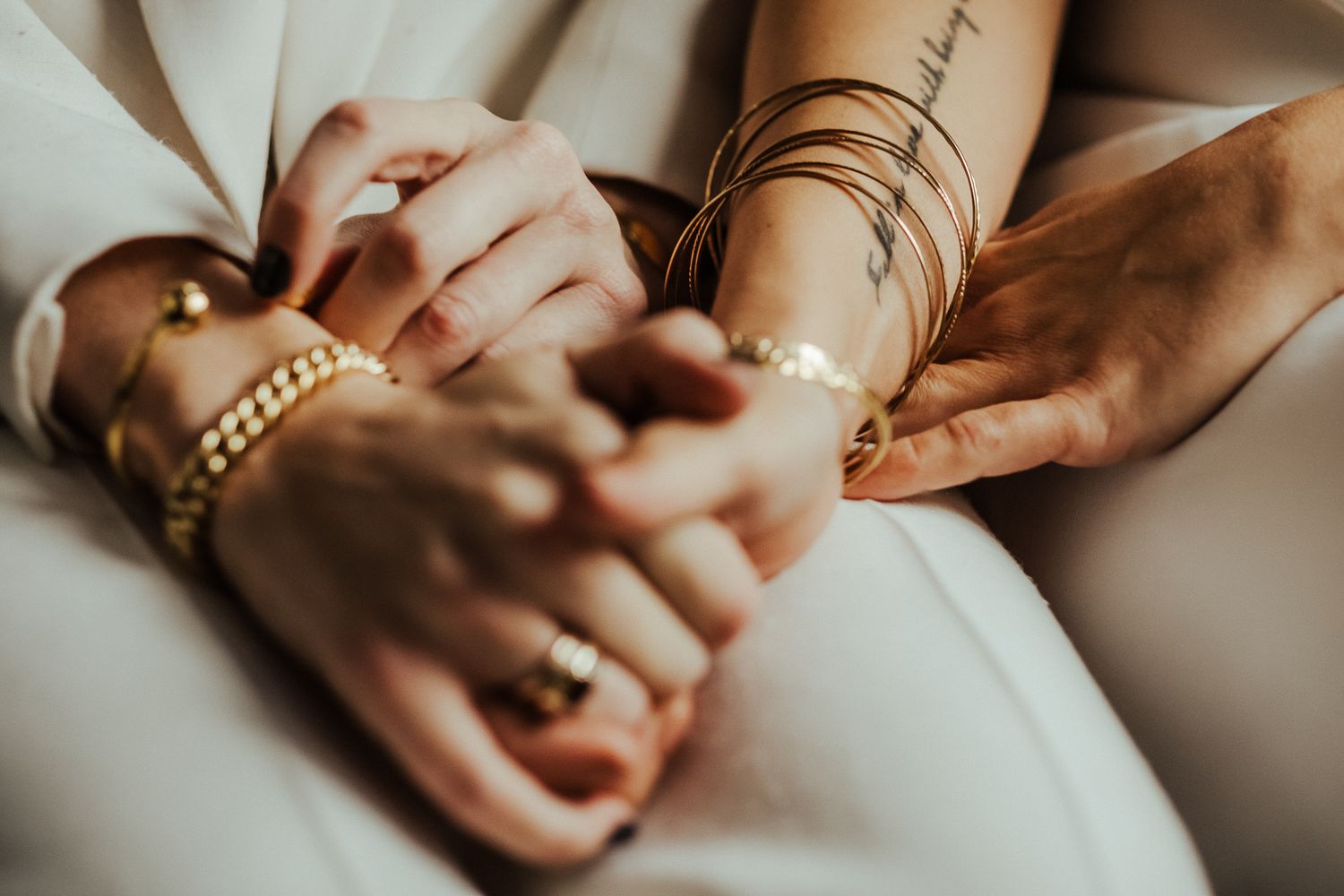 Close-up detail of hands with jewelry and bracelets holding together during a wedding ceremony.