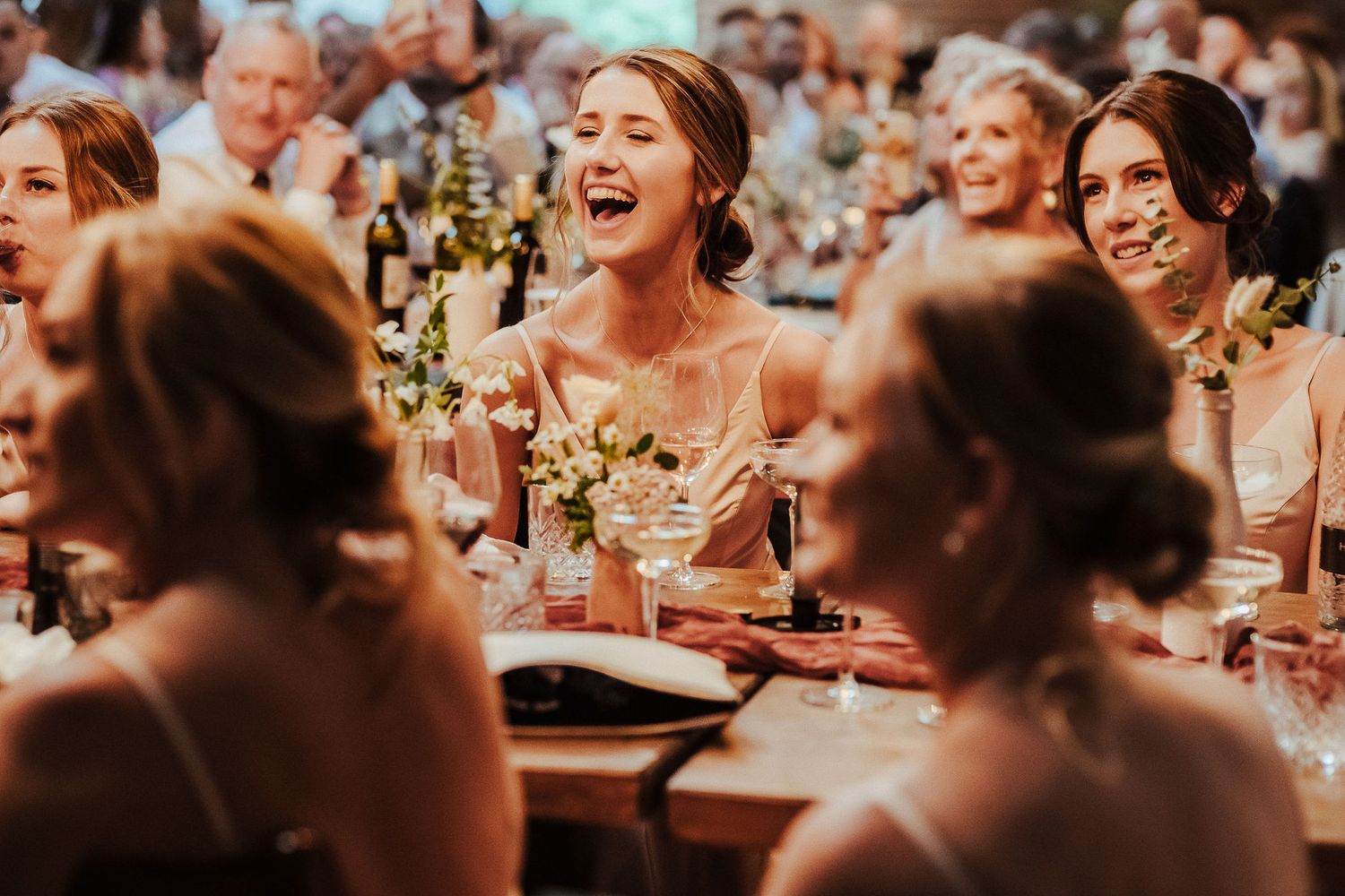 Wedding guests share laughter and excitement during an indoor reception dinner.