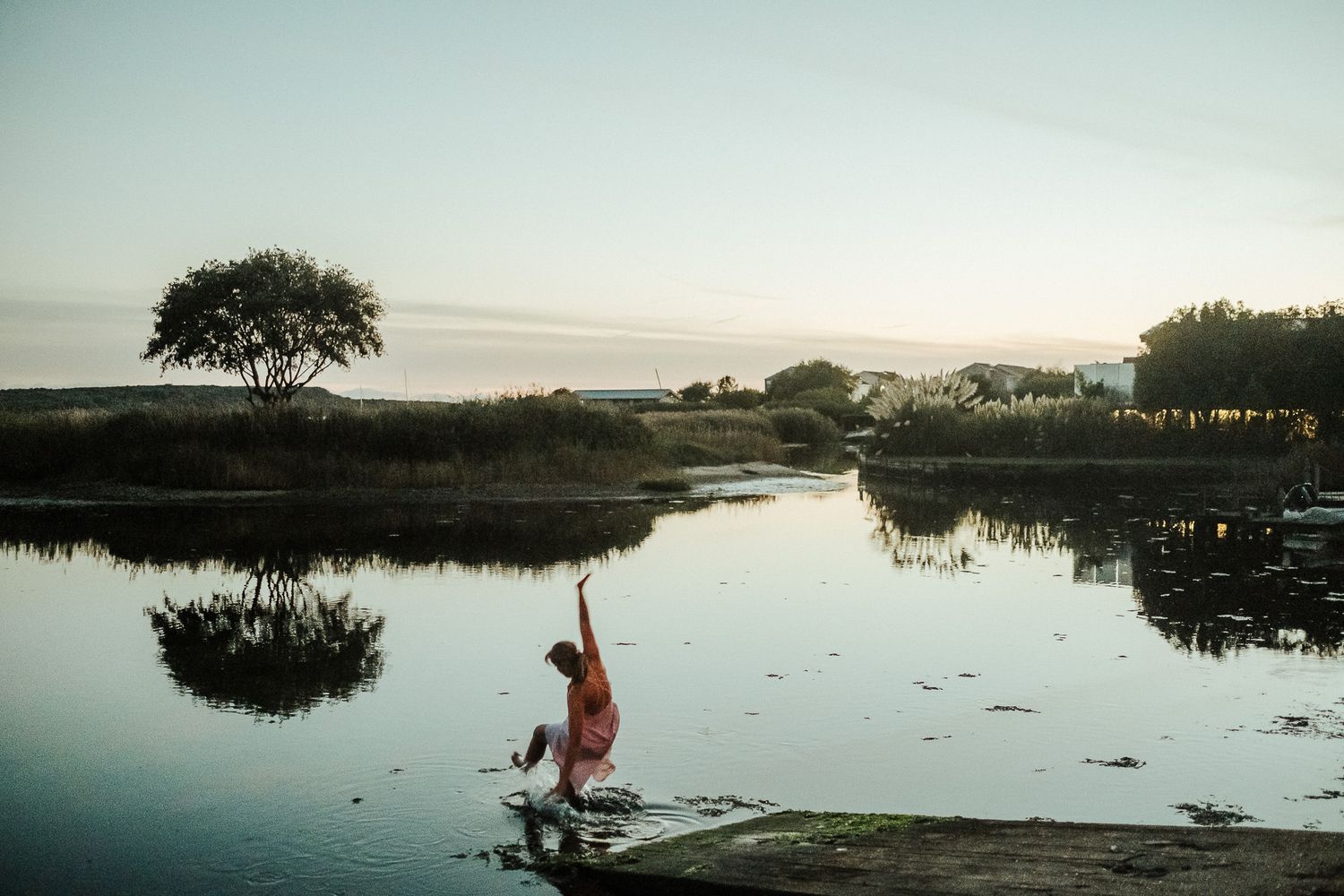 Silhouette of people playing in shallow water during sunset with tree reflections.