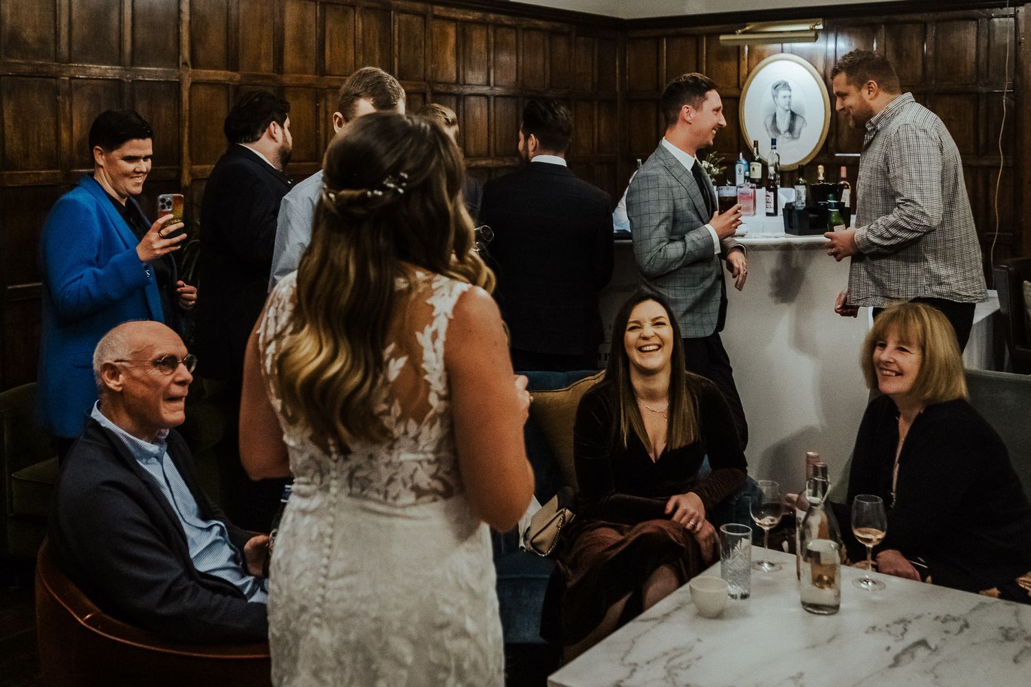 Wedding guests gather in dark wood-paneled room for intimate reception celebration.