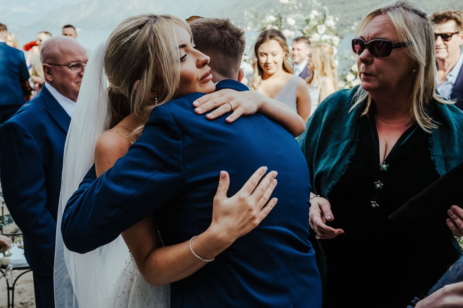 Wedding guests share hugs and congratulations during an outdoor lakeside reception.