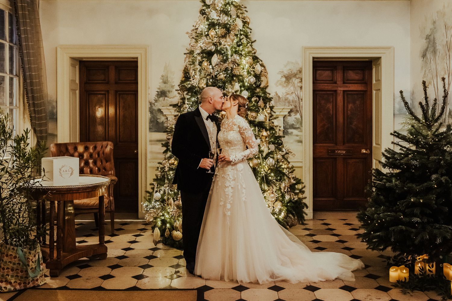 Elegant couple poses in front of illuminated Christmas tree in formal interior setting.