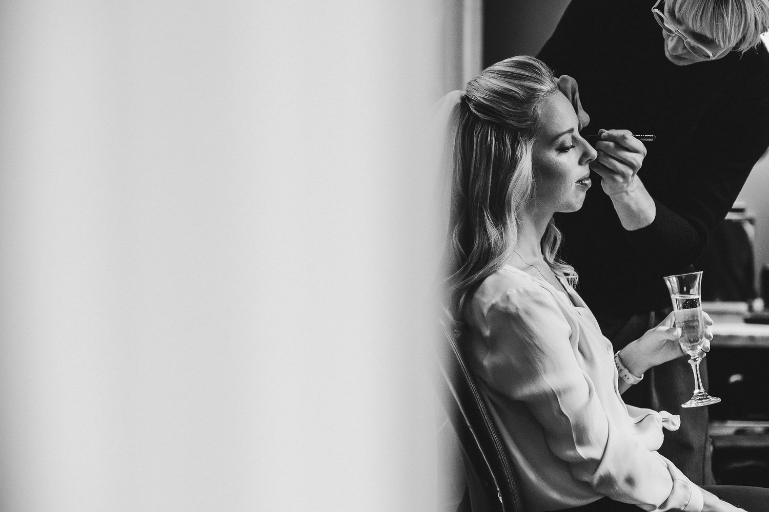 Black and white image of someone having makeup applied during wedding preparations.