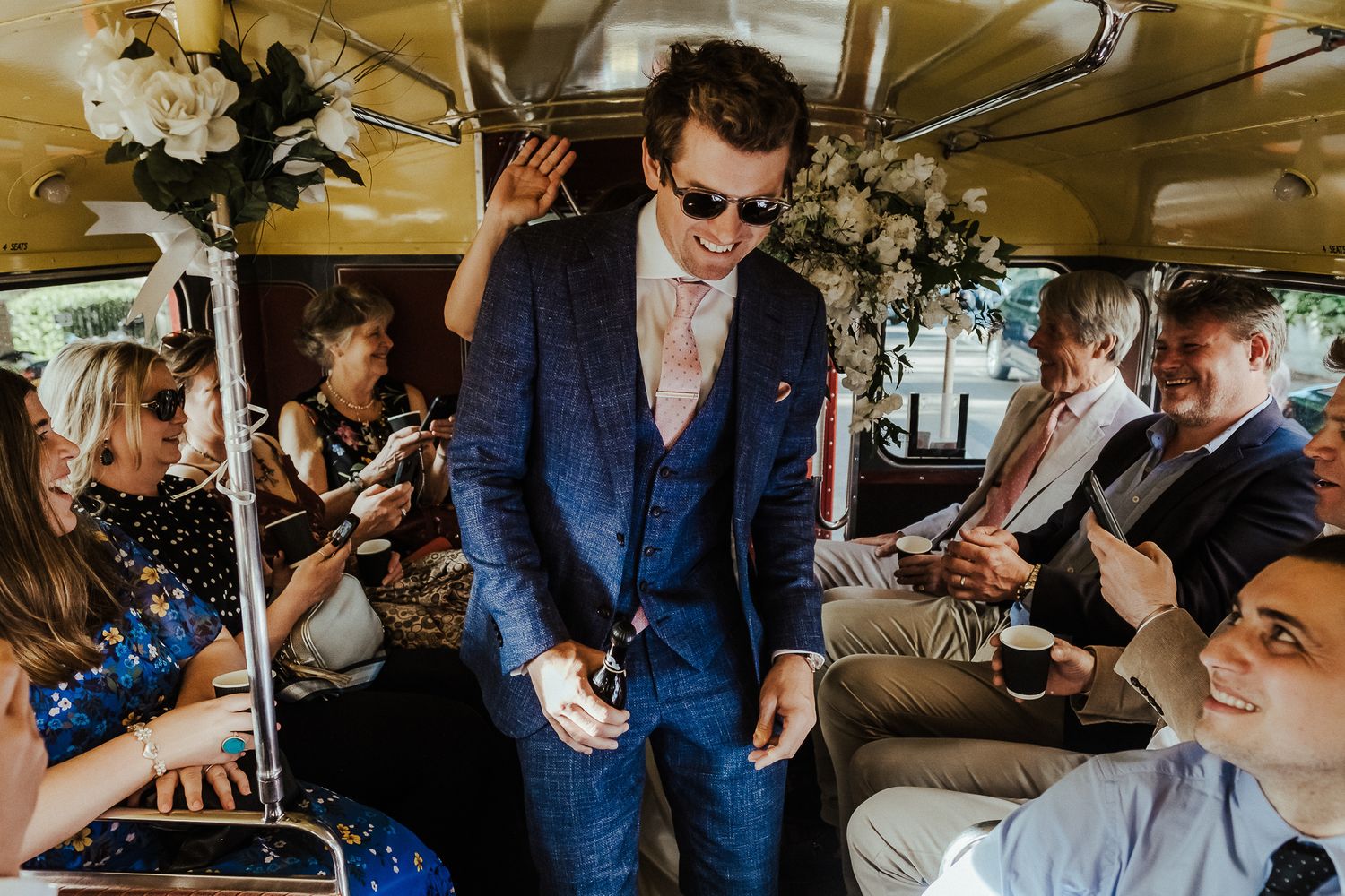 Wedding guests celebrate on a decorated bus with a person dancing in a blue suit.