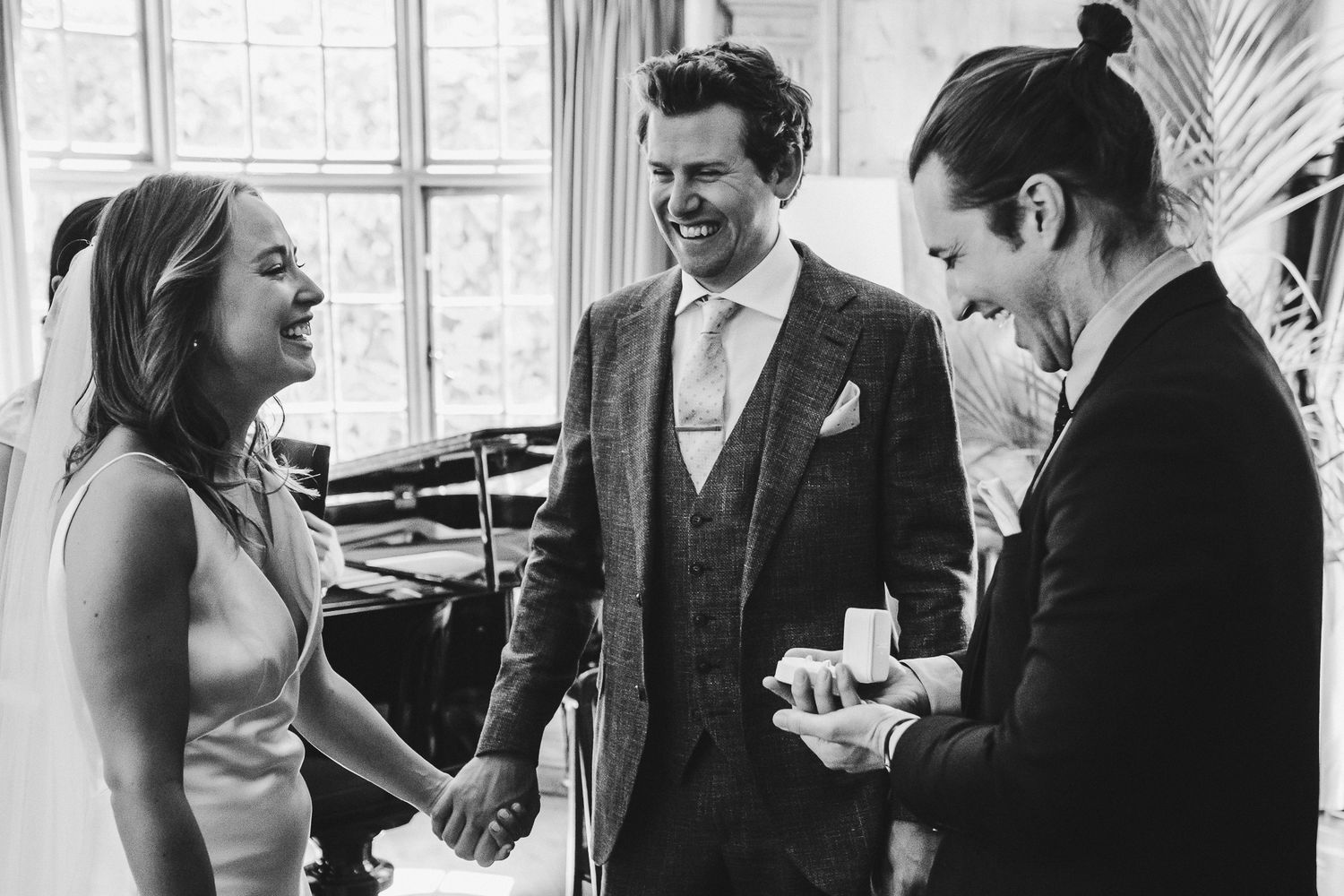 A candid black and white moment of three people sharing laughter during a wedding celebration.
