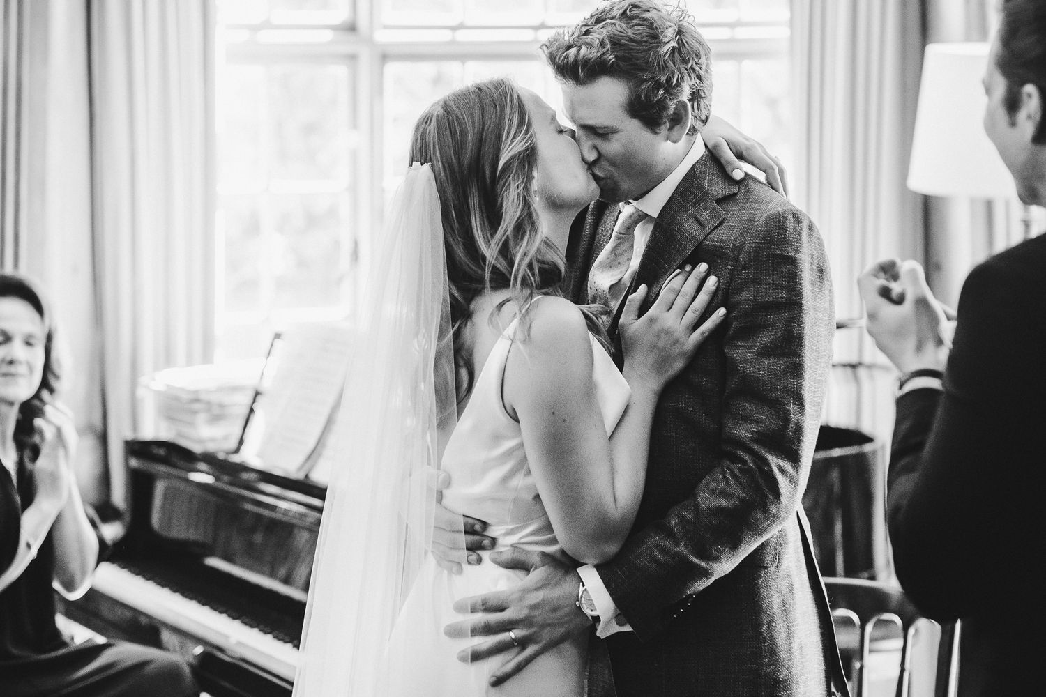 Black and white photo capturing an intimate moment between newlyweds near a piano.