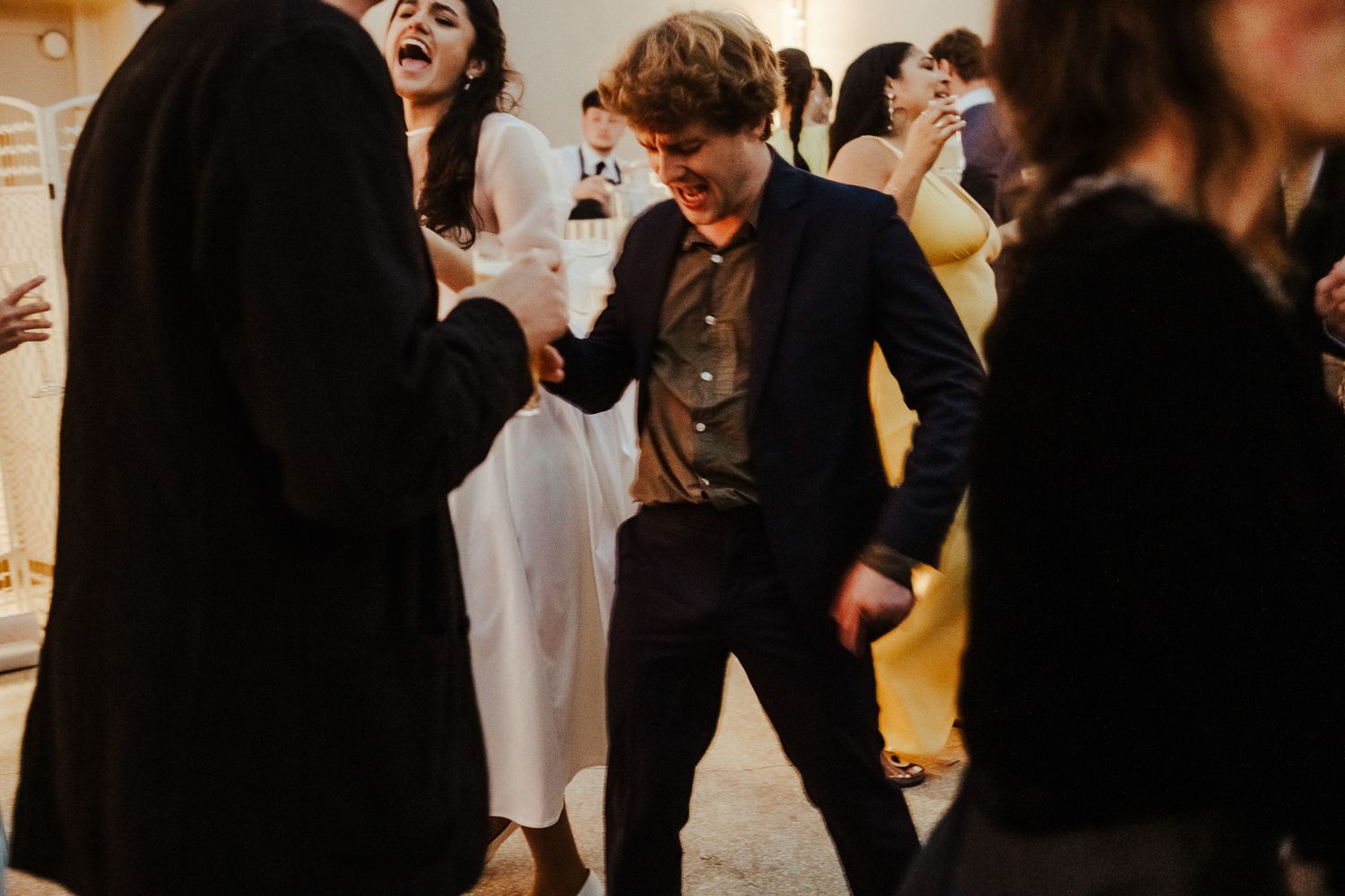 Wedding guests laughing and dancing together during a joyous celebration indoors.