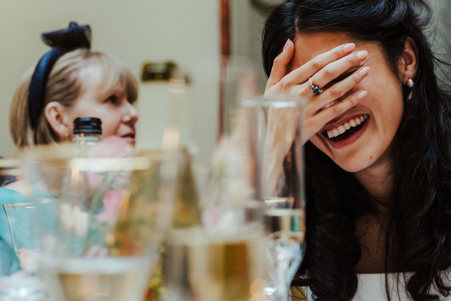 Candid black and white photograph of guests laughing during wedding reception speeches.