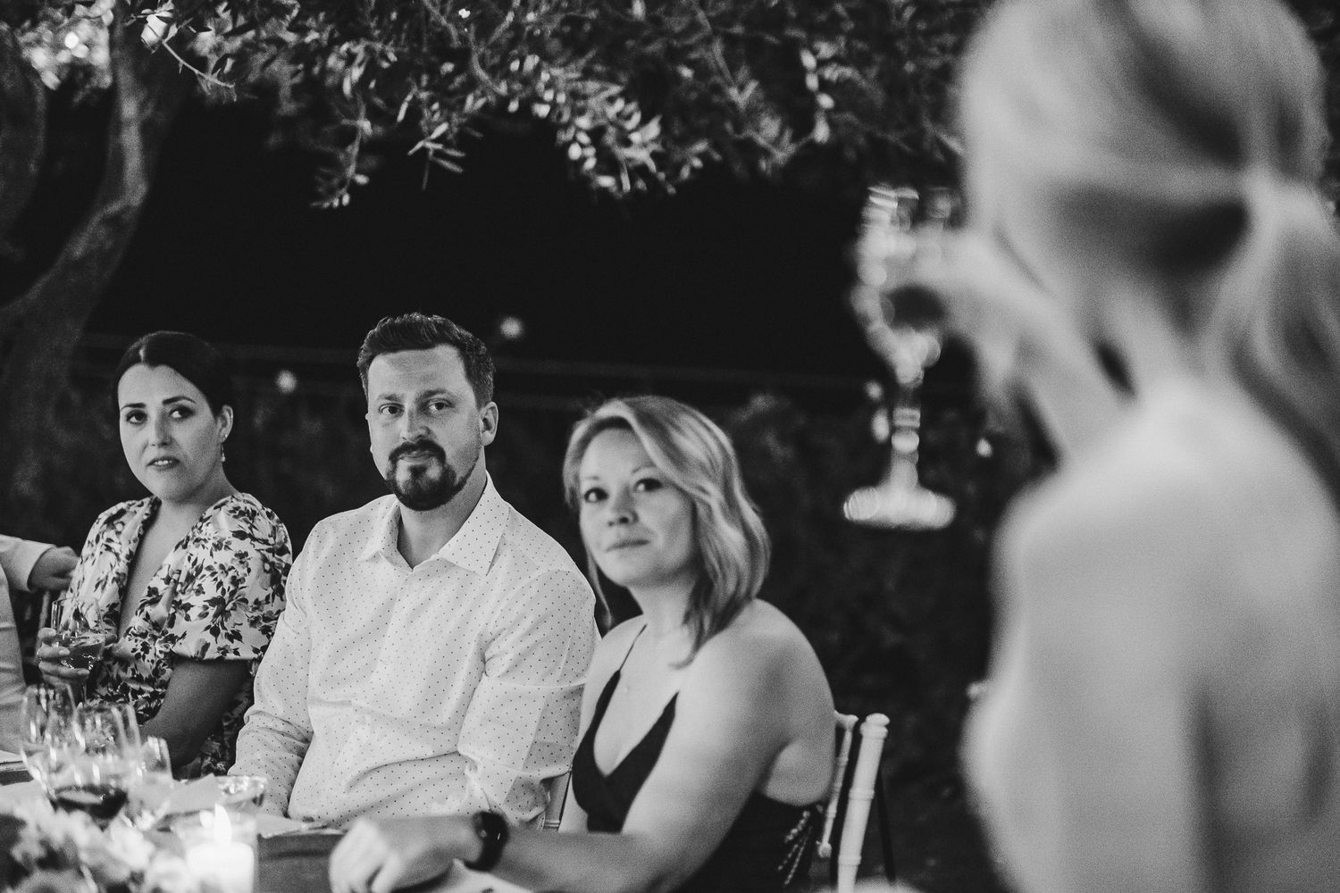 Wedding guests seated at an elegant outdoor dinner table under garden lights.