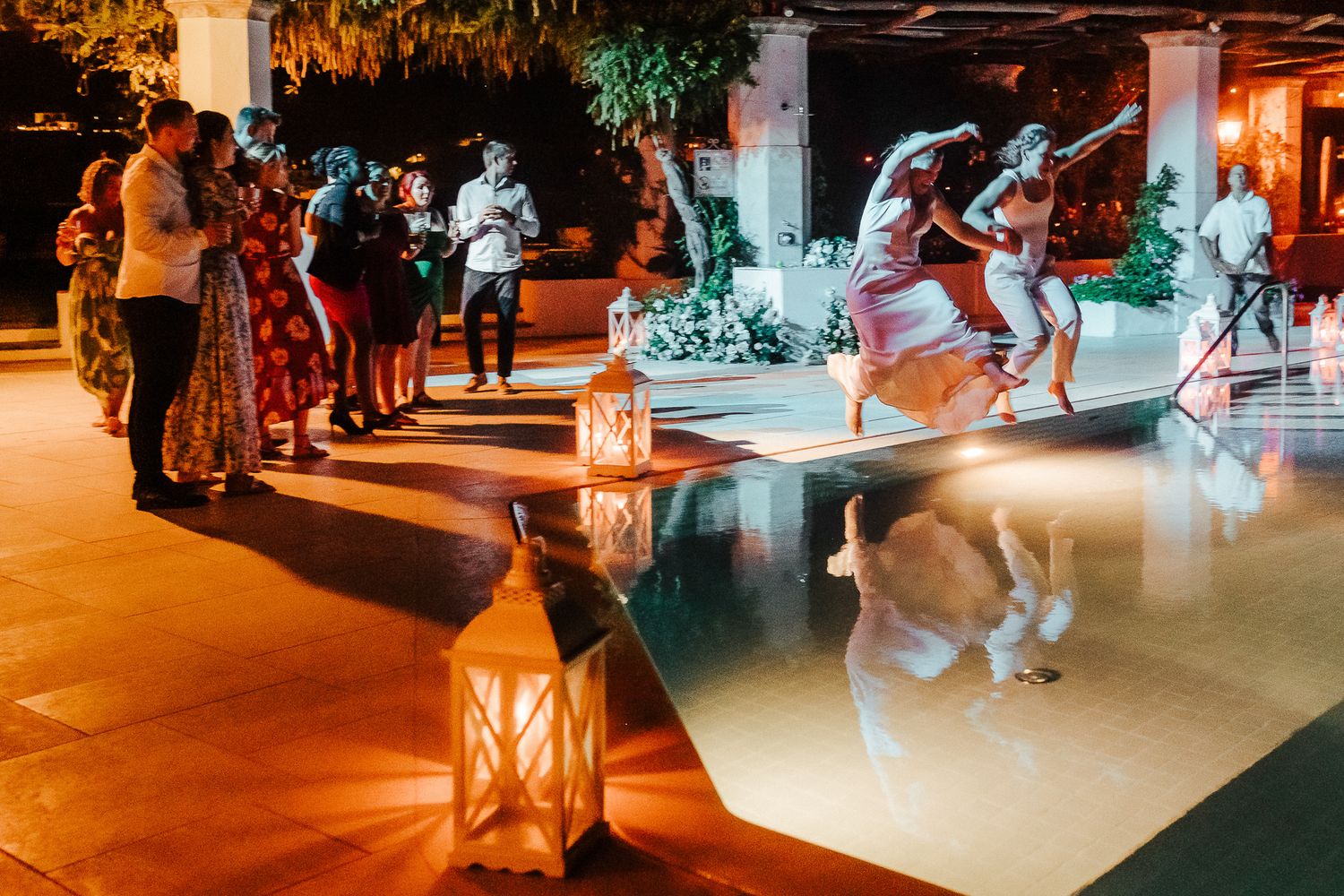 People dancing and celebrating around a poolside venue with lantern lighting.