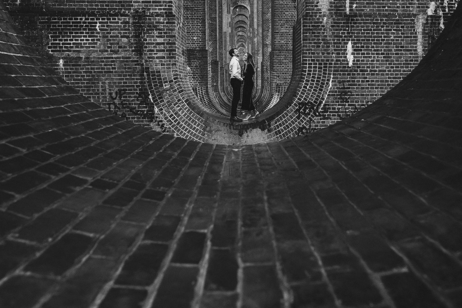 Architectural black and white photo of a curved brick tunnel with arches.