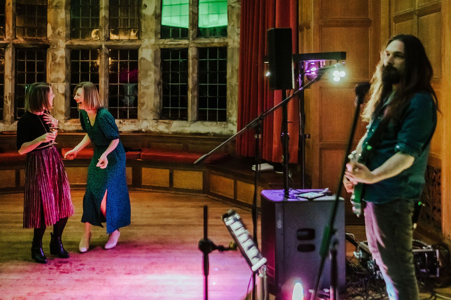 Musicians performing on stage with pink and purple lighting in an ornate vintage hall.