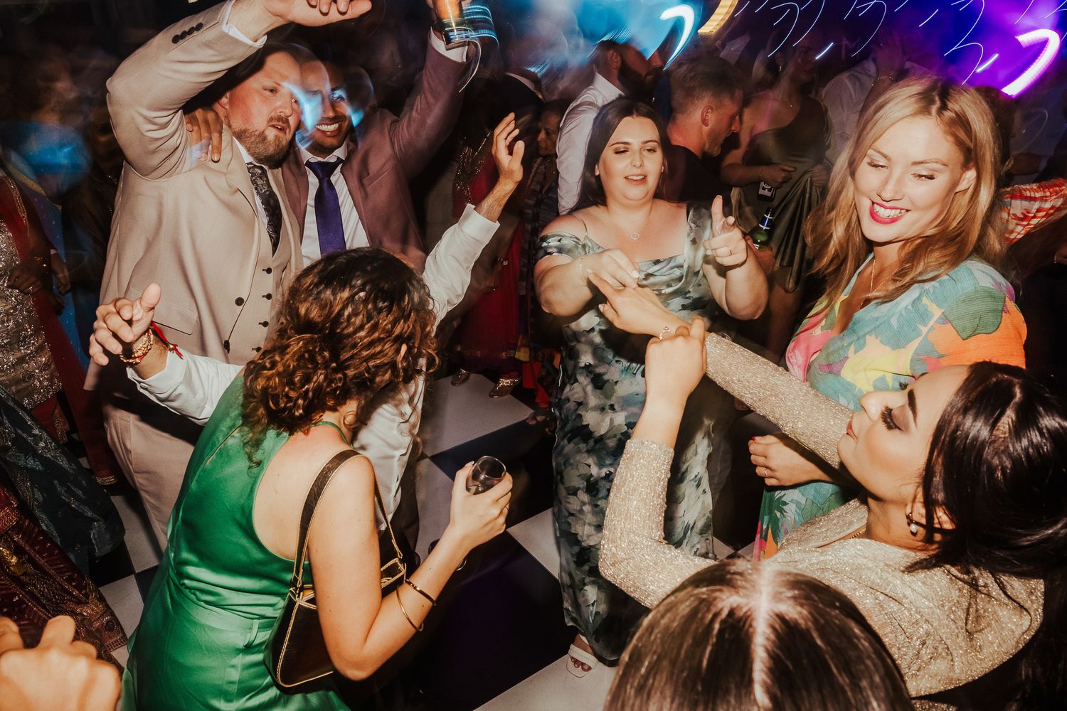 People dancing and celebrating at a dimly lit nighttime party event with colorful lighting effects.
