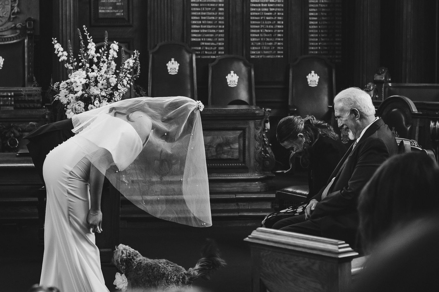 Black and white photo shows dancers performing choreographed moves in an elegant vintage interior setting.