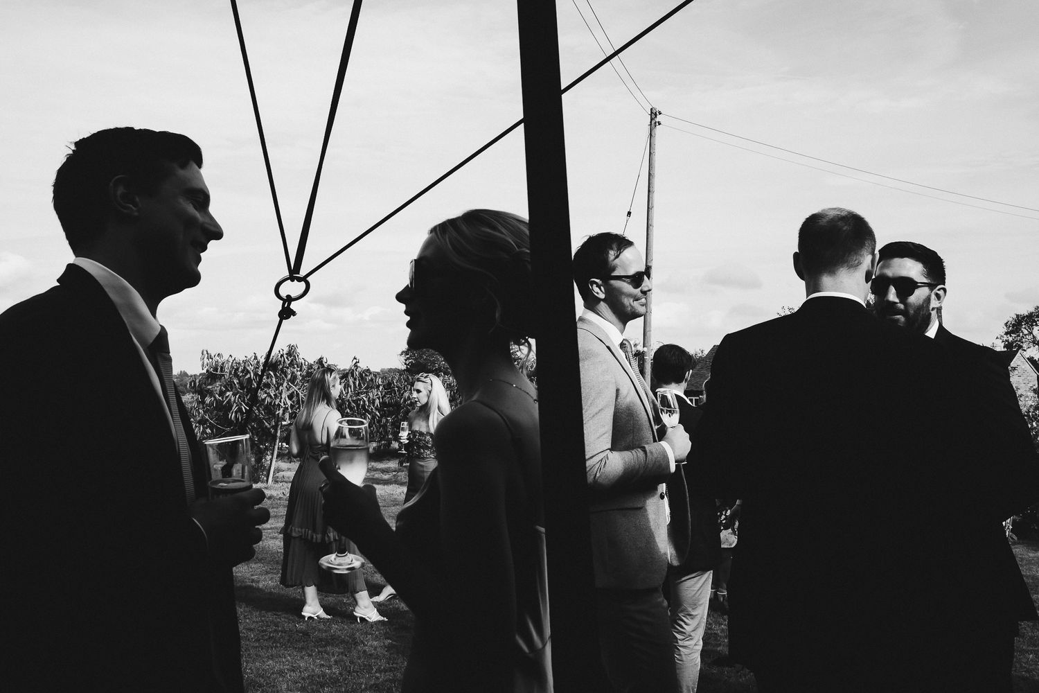 Black and white photo of wedding guests gathered under umbrellas outdoors.
