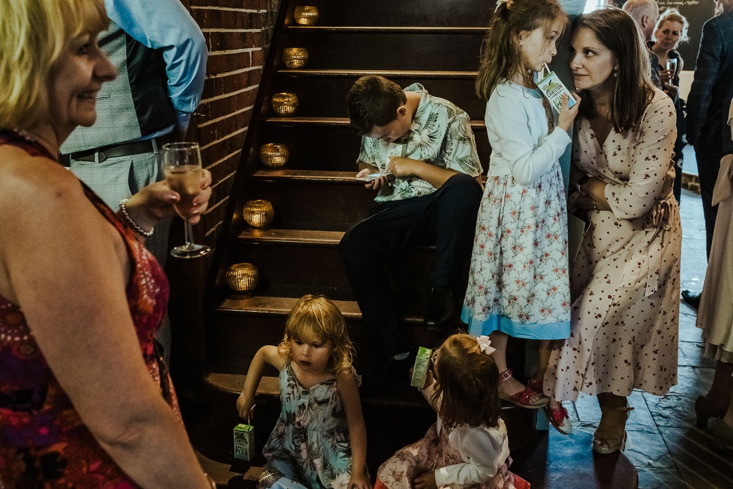 Wedding guests and children gather on vintage wooden staircase during reception.