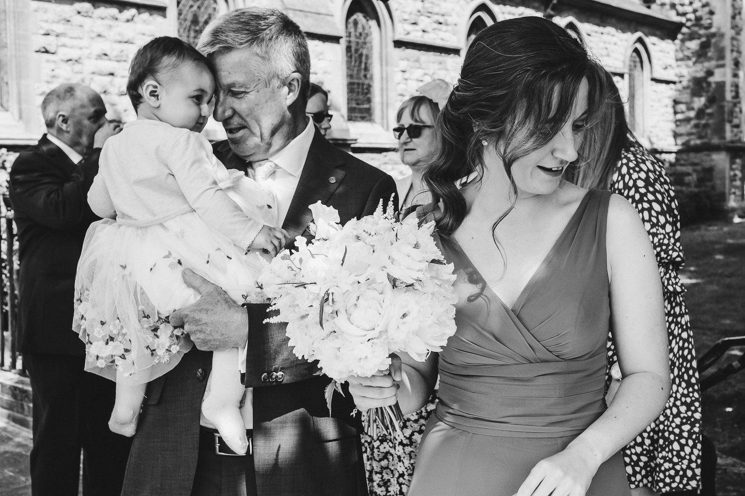 A gathering outside a stone church with elegant floral bouquets and formal attire.