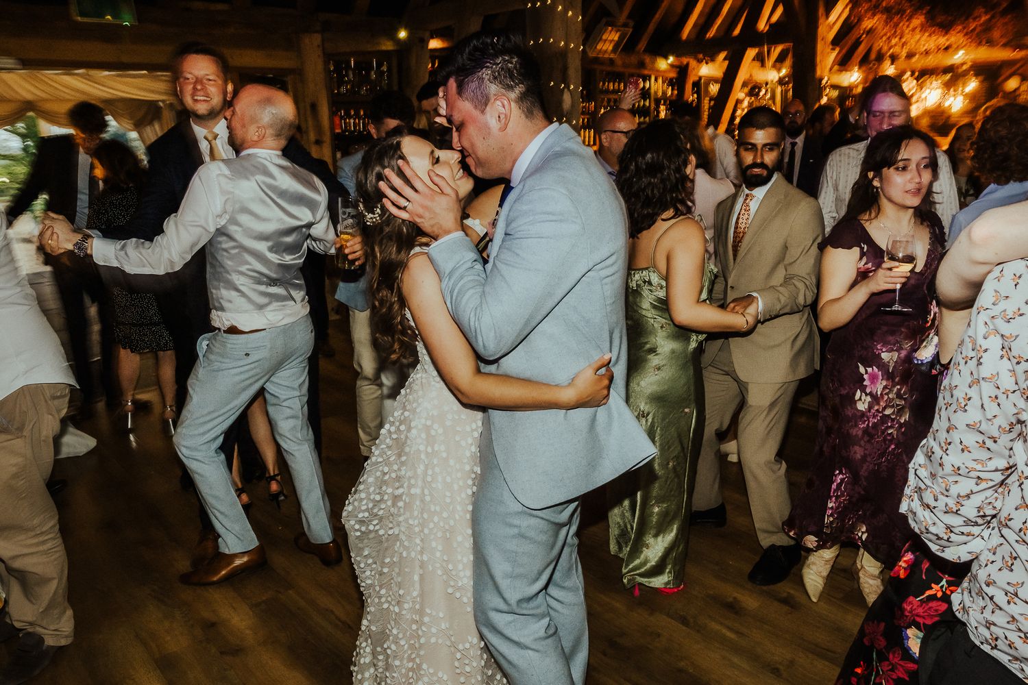 Wedding guests dancing and celebrating on a rustic wooden dance floor.