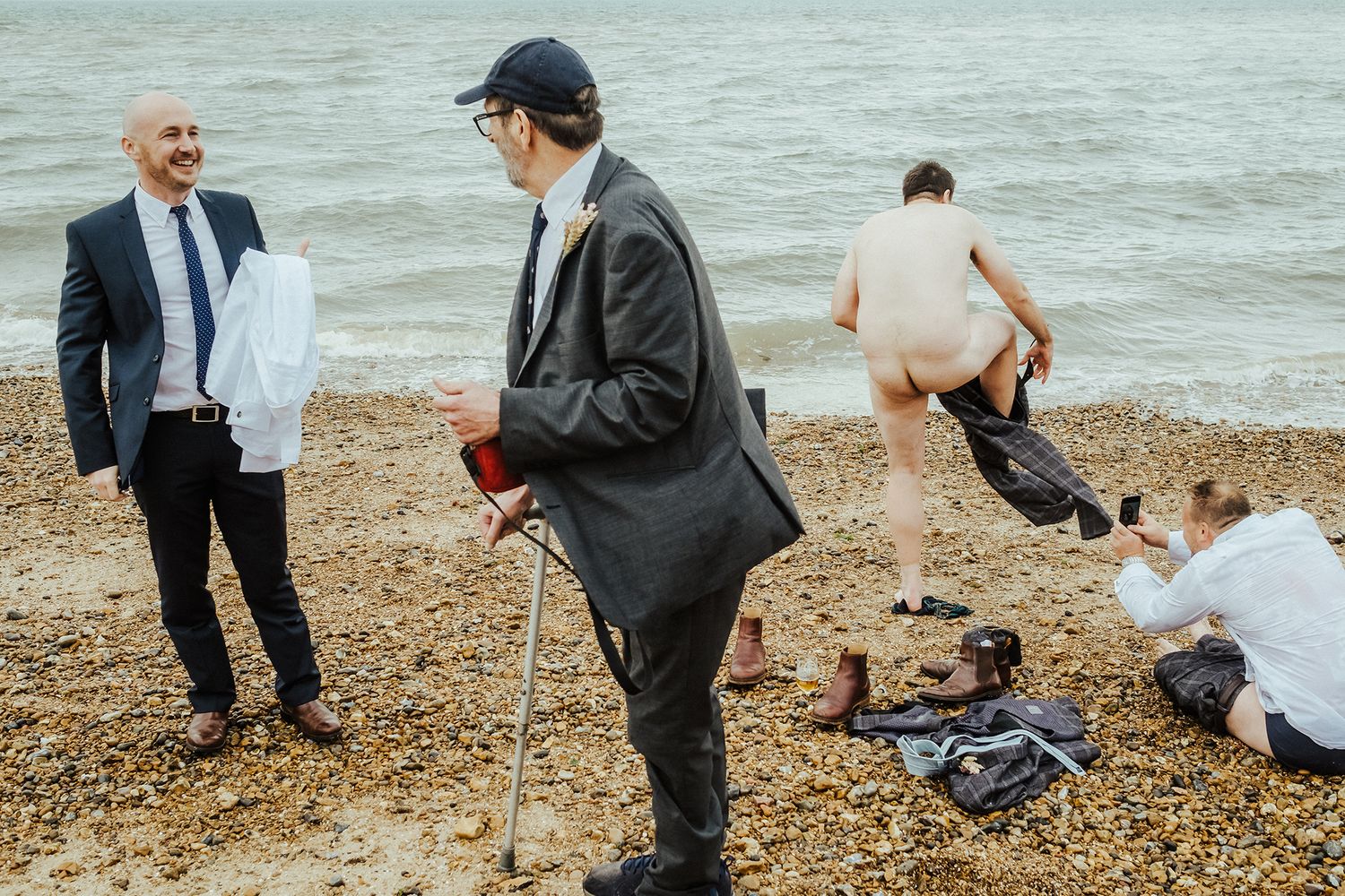 Beach wedding scene with guests and couple enjoying casual moments by the water.