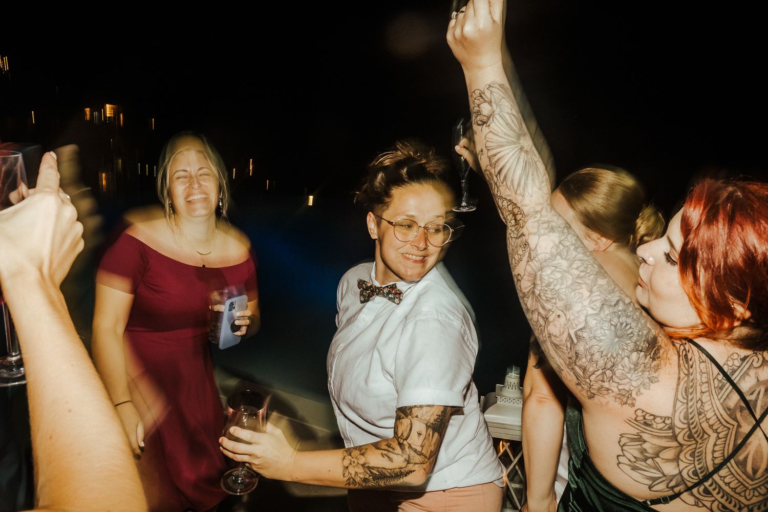 Lively reception guests dancing with drinks in hand at a dimly lit party.