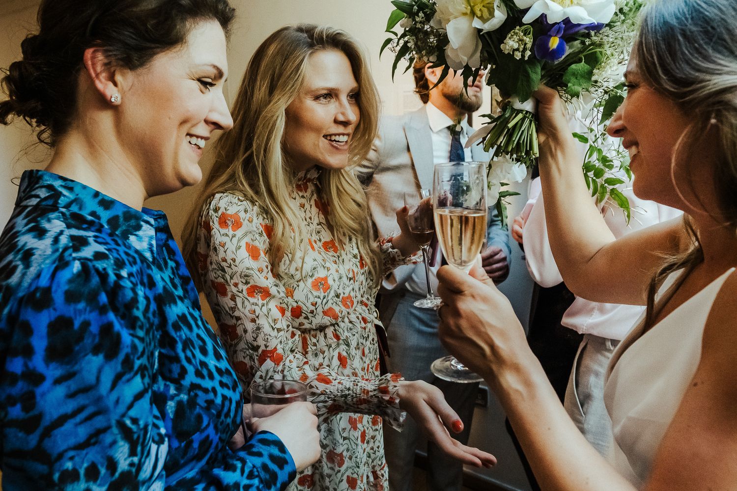 Wedding guests in colorful attire share champagne and laughter at a reception.